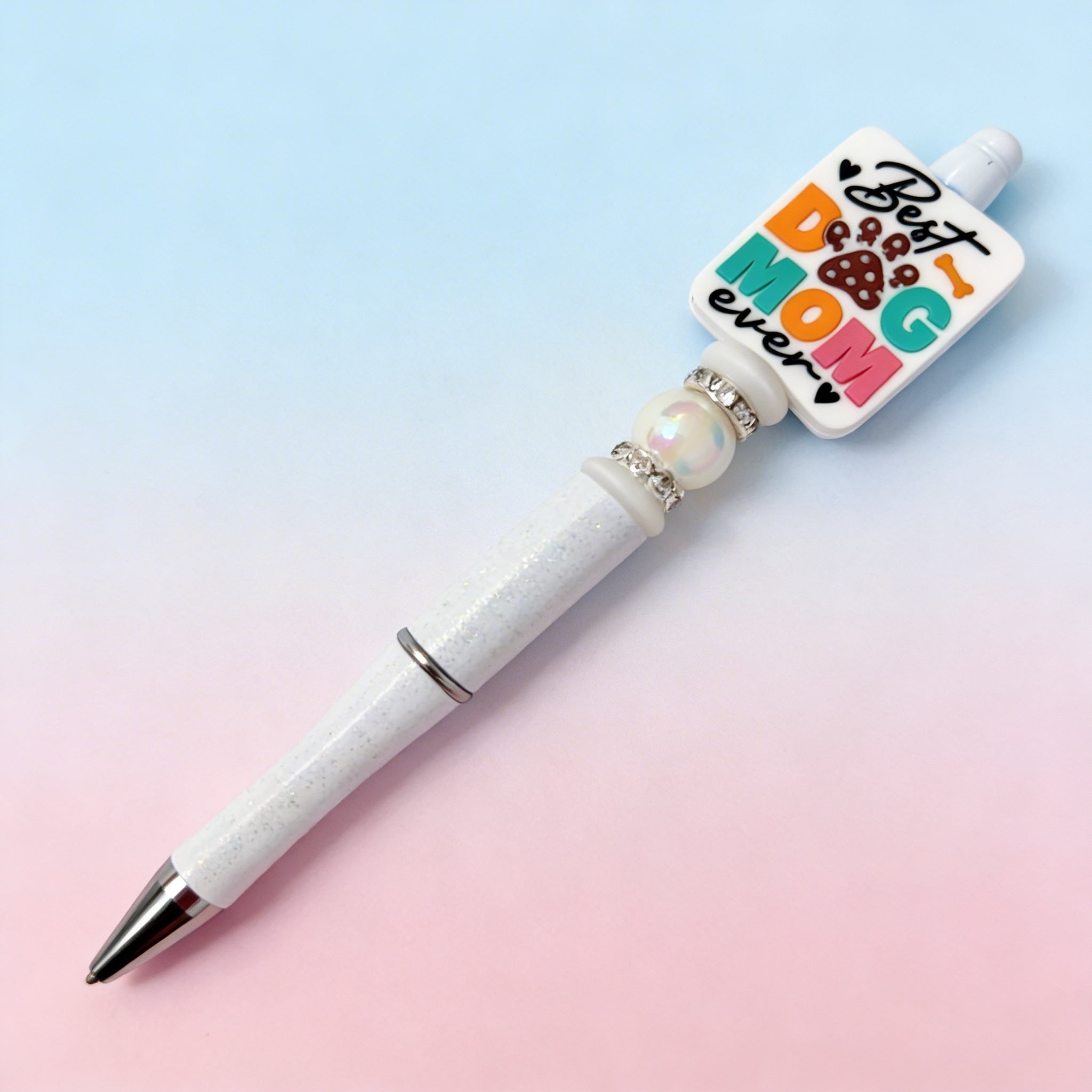 Pen with a decorative top that reads 'Best Dog Mom ever' on a beige background