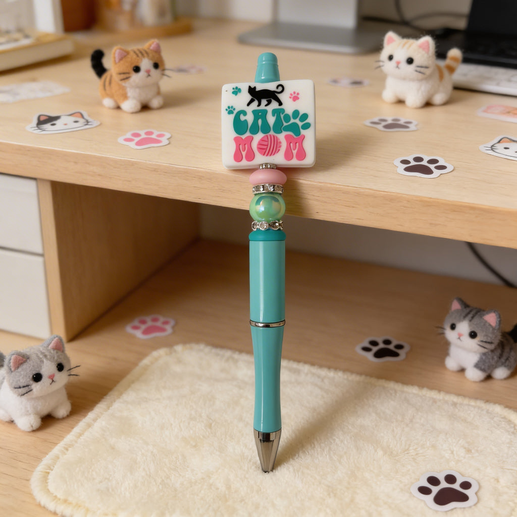 Turquoise pen with 'Cat Mom' stamp on a desk with cat-themed decorations