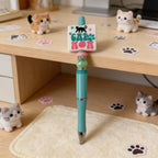 Turquoise pen with 'Cat Mom' stamp on a desk with cat-themed decorations