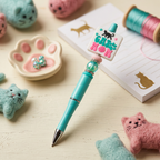 Turquoise pen with cat-themed design on a surface with cat-themed items
