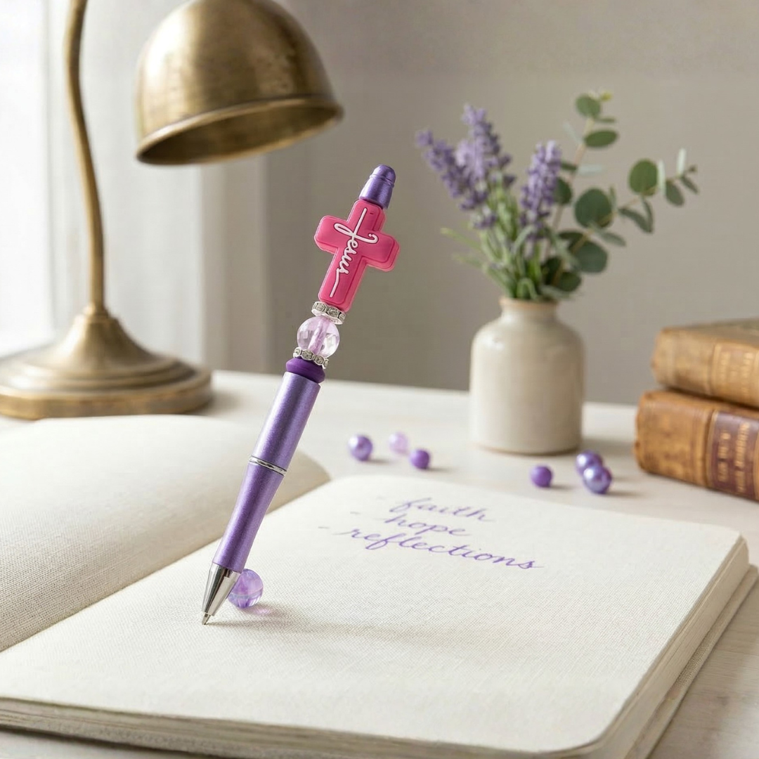 Purple pen with cross design on a notebook next to a vase of flowers and books.
