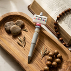 Pen with motivational message on top of a wooden tray with stones and a book.