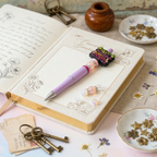 Decorative pen with decorative elements on an open notebook with keys and small items around.