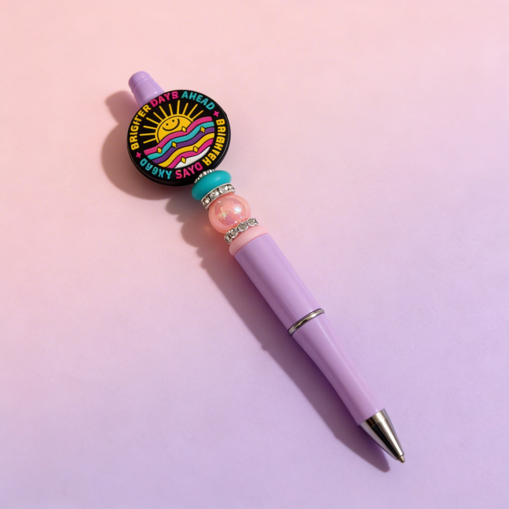Decorative pen with colorful bead accents on a gradient pink background