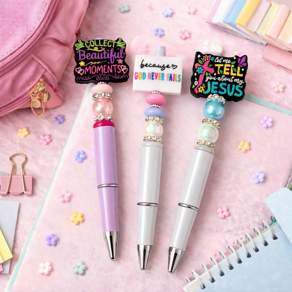 Three decorative pens with motivational text on a pink background with stationery items.