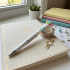 Pen, decorative tape, and rabbit-shaped clip on a notebook with a window and plant in the background